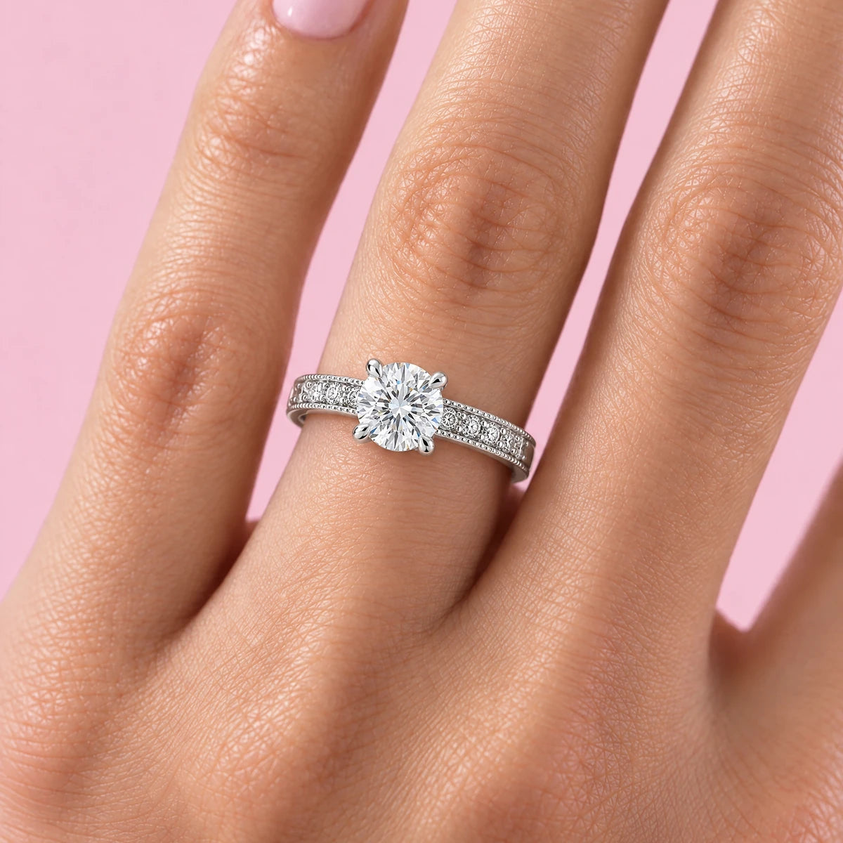 Classico milgrain solitaire moissanite ring worn on the ring finger, pink background